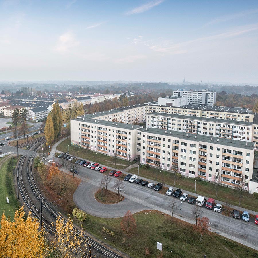 Das Foto zeigt den Ausblick auf die Von-Stauffenberg-Straße. Zu sehen ist eine Wohnsiedlung mit mehreren mehrgeschossigen Plattenbauten in urbaner Umgebung, angrenzend an Straßenbahntrasse und Parkflächen, herbstliche Stimmung mit Laubbäumen.