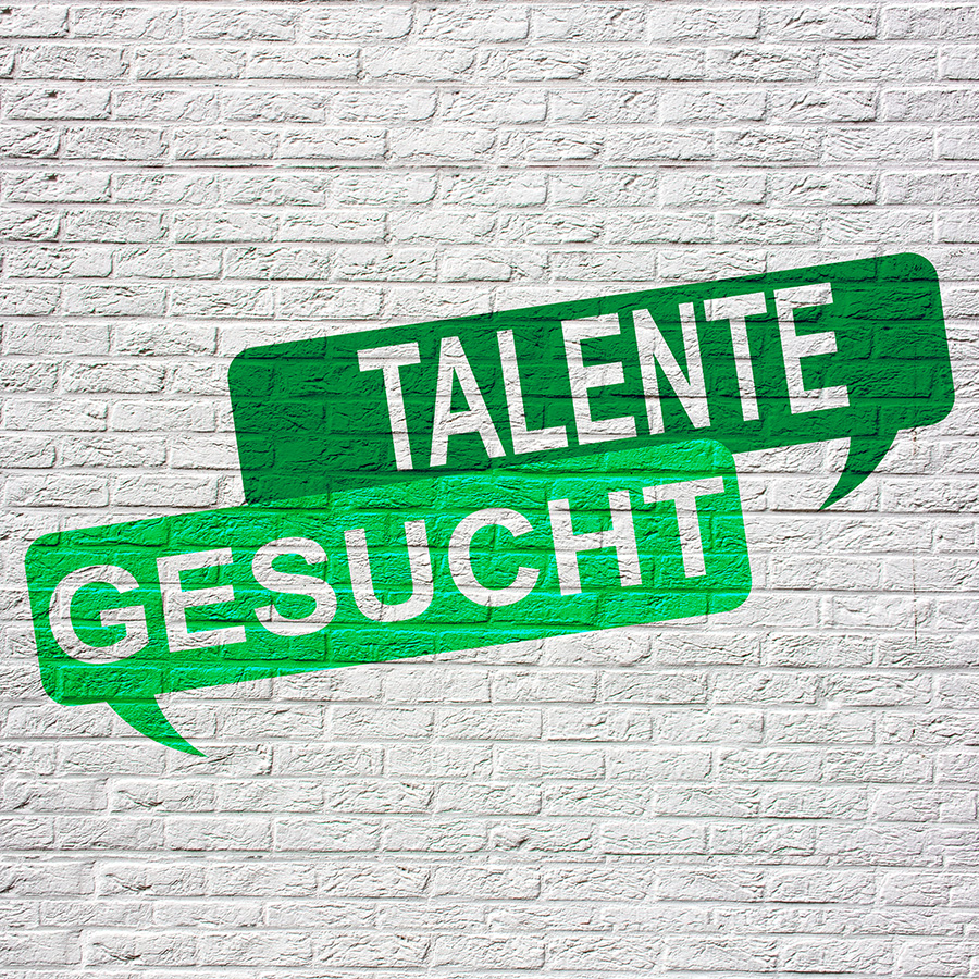 Grüne Sprechblasen mit weißer Schrift ‚Talente gesucht‘ auf einer weißen Backsteinwand – Hinweis auf Ausbildungsmöglichkeiten.