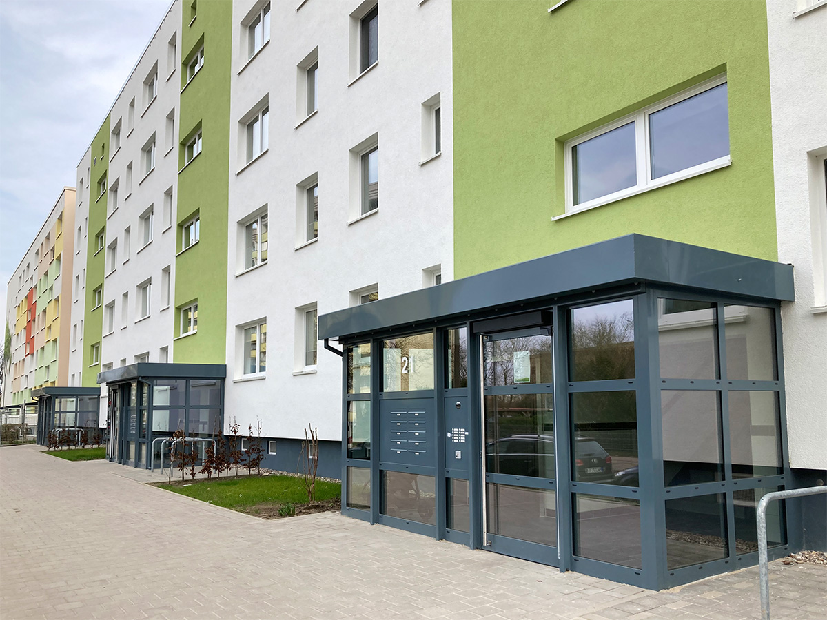 Das Foto zeigt den Hauseingangsbereich in der Anne-Frank-Straße 21-23. Der Glasvorbau wirkt sehr modern und verleiht den Wohngebäude ein attrakives Aussehen.