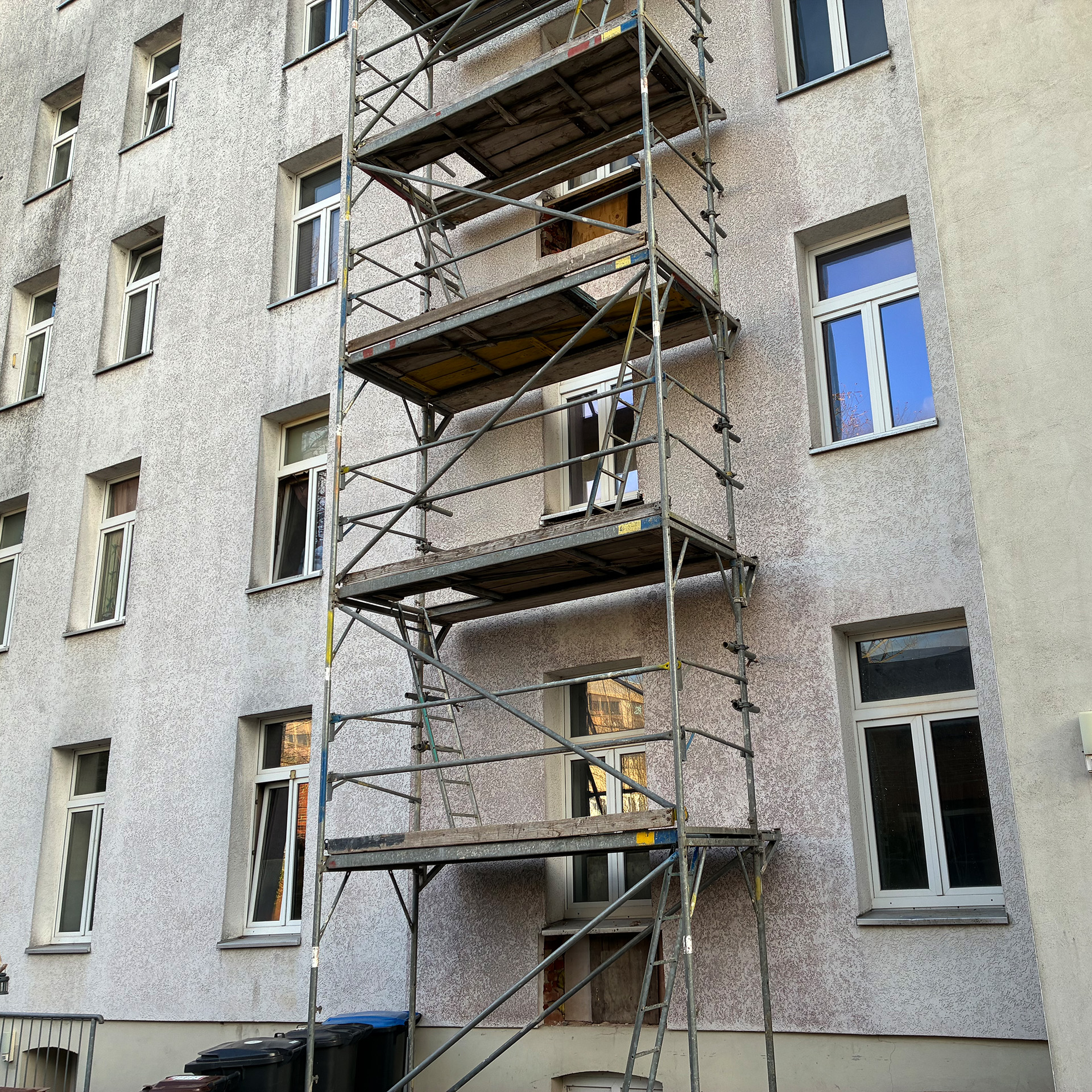 Mehrfamilienhaus mit Fassadengerüst während Bauarbeiten, mehrere Fenster sichtbar – Außenansicht einer laufenden Sanierung. Das Bild zeigt den Anbau der Balkone.